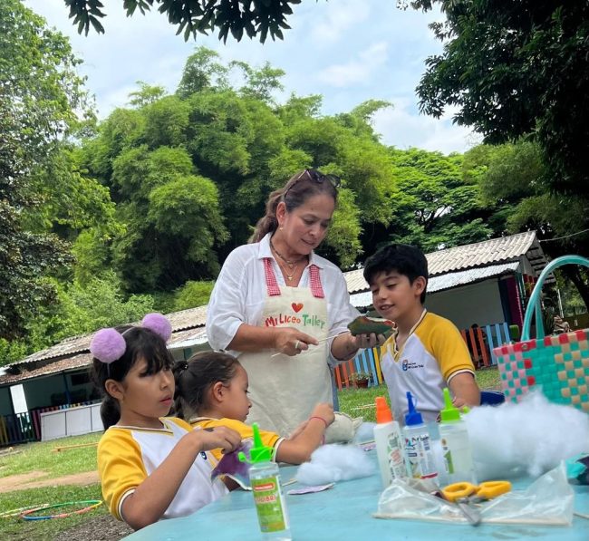 Docente y estudiantes de educación inicial realizan una actividad de manualidades con pegamento, algodón y materiales creativos en un espacio al aire libre rodeado de naturaleza